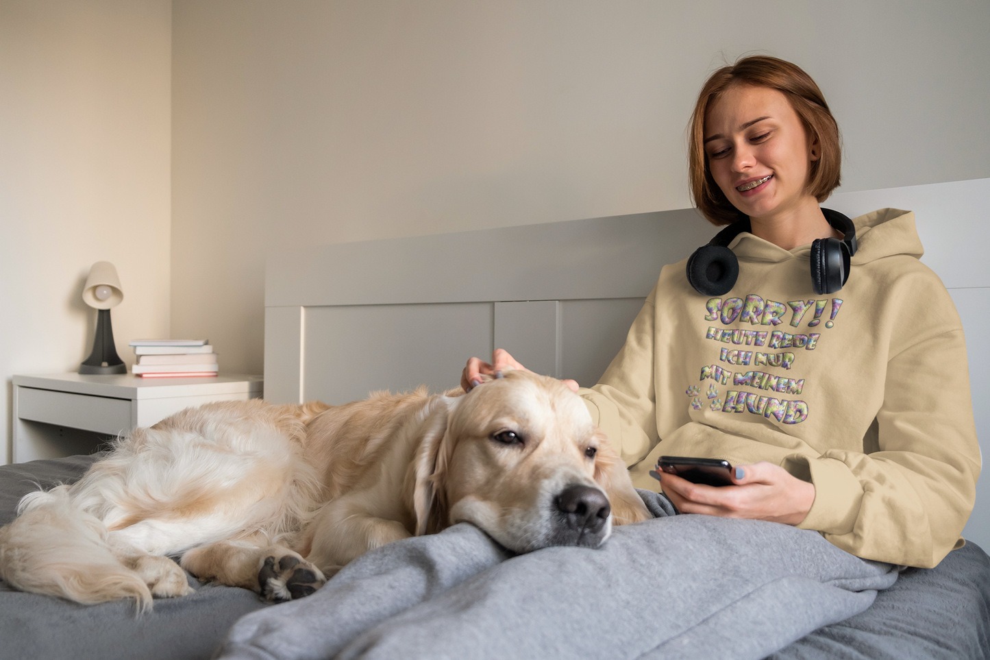 Frau trägt einen bunten Hoodie für Hundeliebhaber von Milkis Way und sitzt mit goldenem Retriever im Bett