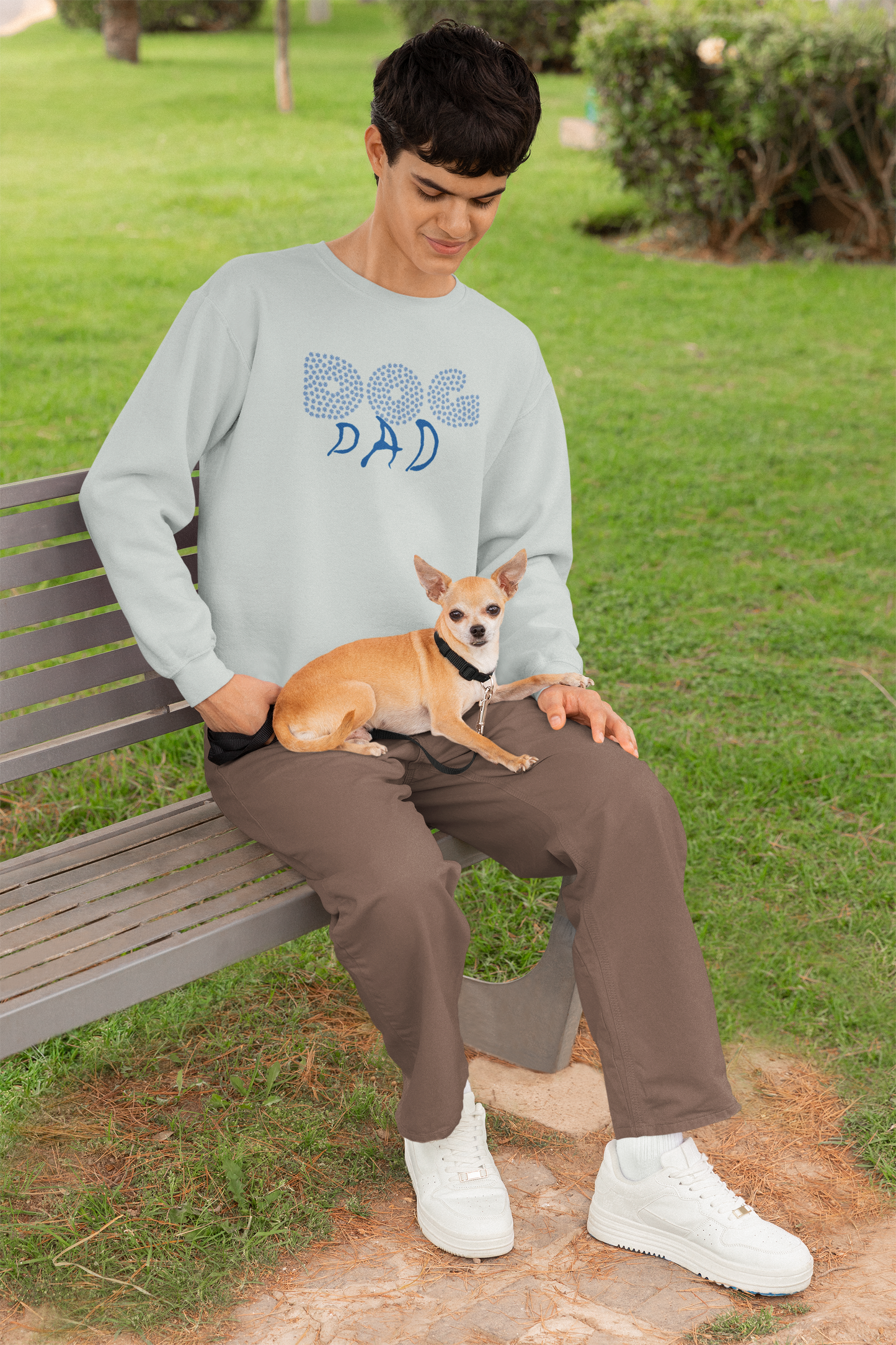 Milkis Way Sweatshirt mit Hundepfote Print getragen von sitzendem Mann mit kleinem Hund auf dem Schoß im Park