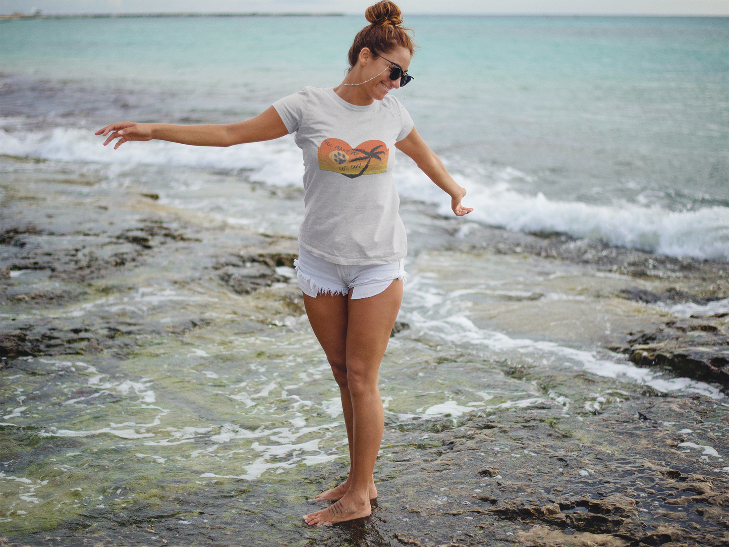 Unisex T-Shirt mit Hundepfoten Print von Milkis Way, getragen am Strand von Frau mit Sonnenbrille